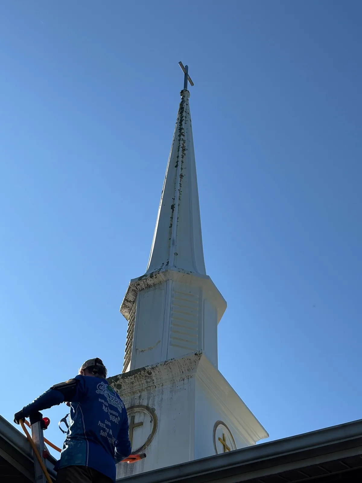 Stand Out crew member looking up at a church steeple streaked with green algae in Denver NC