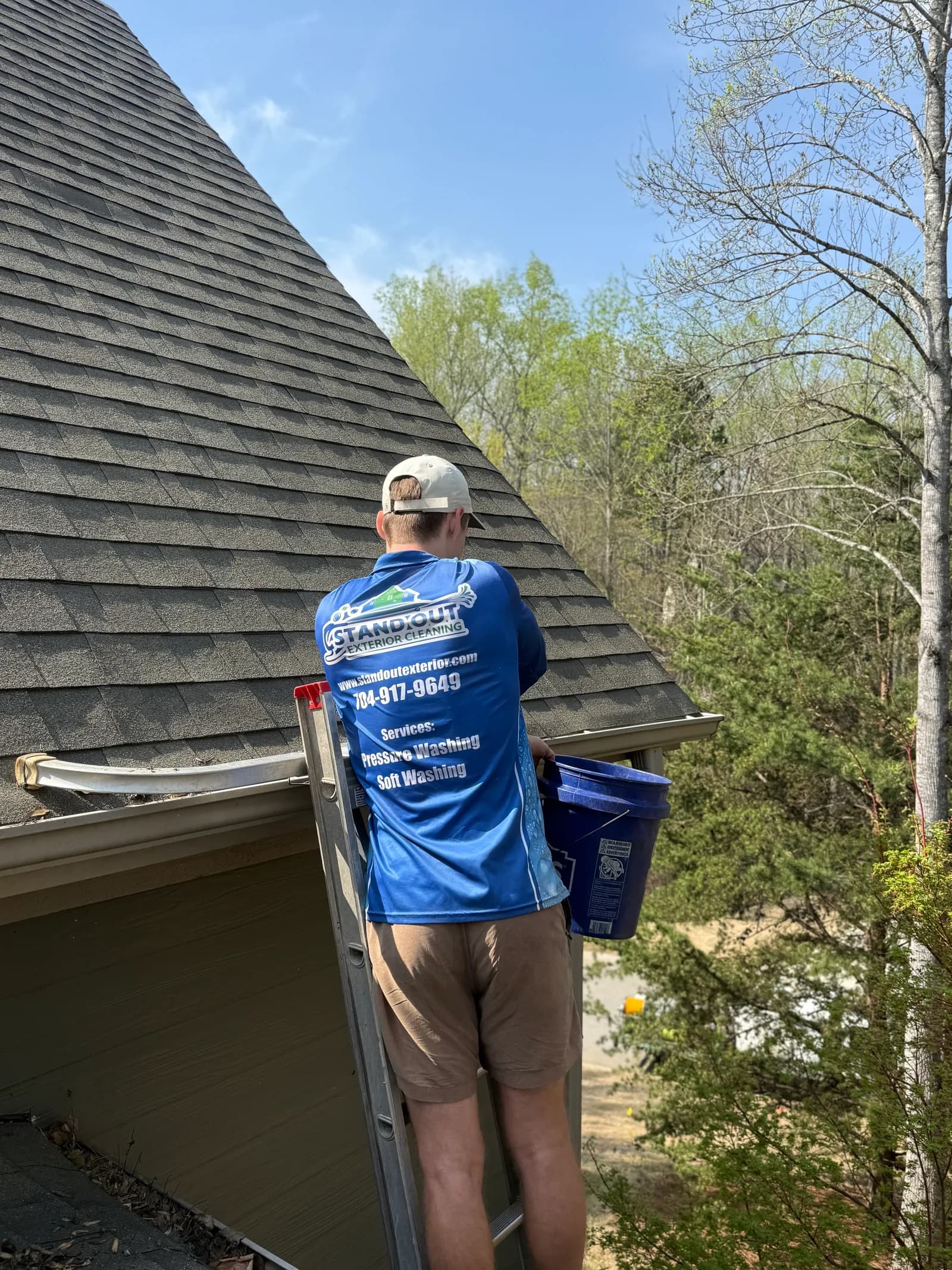 Stand Out Exterior technician cleaning a clogged gutter from a ladder on a home in Cornelius NC